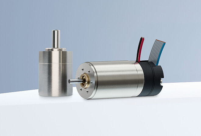 直径为 16 mm 的 FAULHABER 直流电机、减速机和编码器 - 封头 两台 FAULHABER SXR 和 GXR 系列直流电机和一个编码器,排列在灰蓝色背景下的白色平台上。